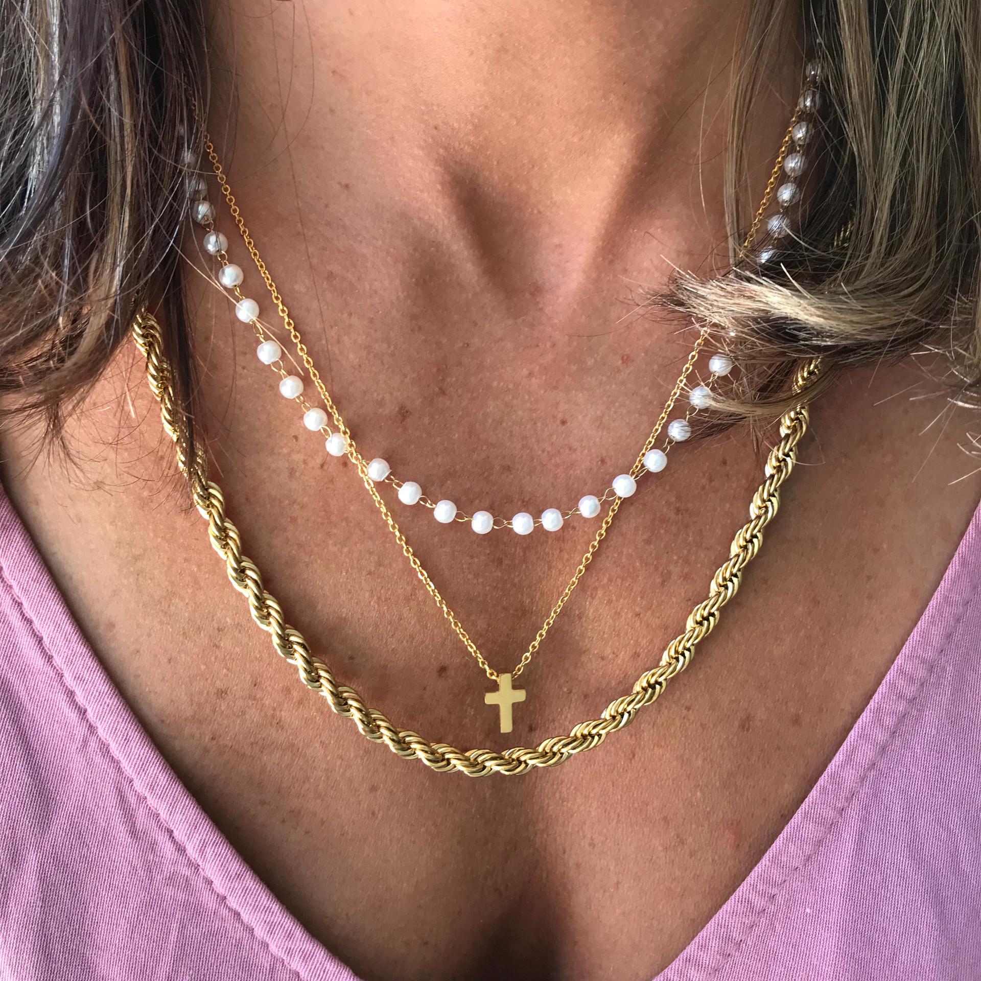 Colares femininos com pérolas brancas e correntes douradas com pingente de cruz sobre blusa rosa claro