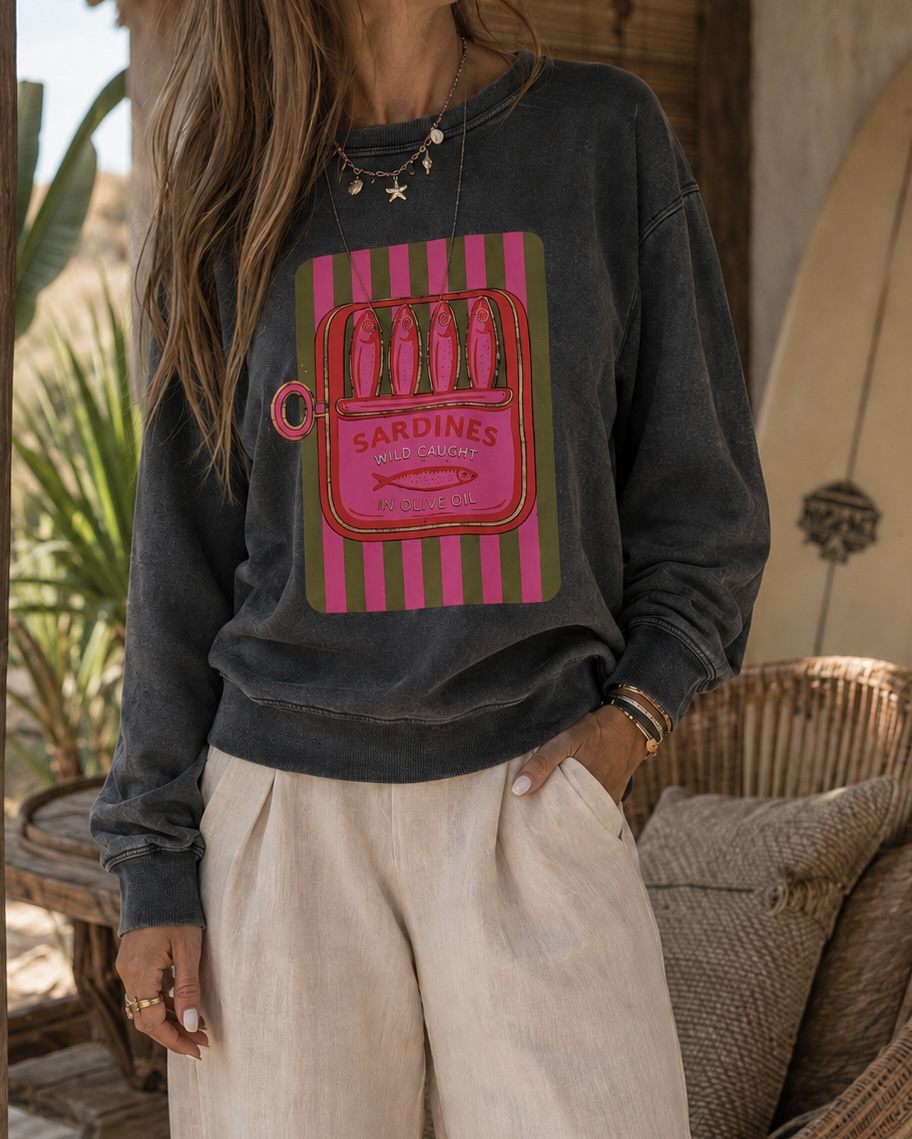 Homem com sweatshirt preta estampada e calças largas bege em ambiente com móveis em vime