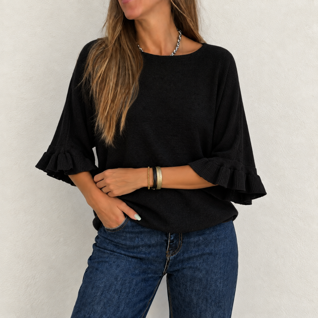 Blusa preta com mangas 3/4 e babados combinada com jeans azul escuro, mulher com acessórios, fundo branco