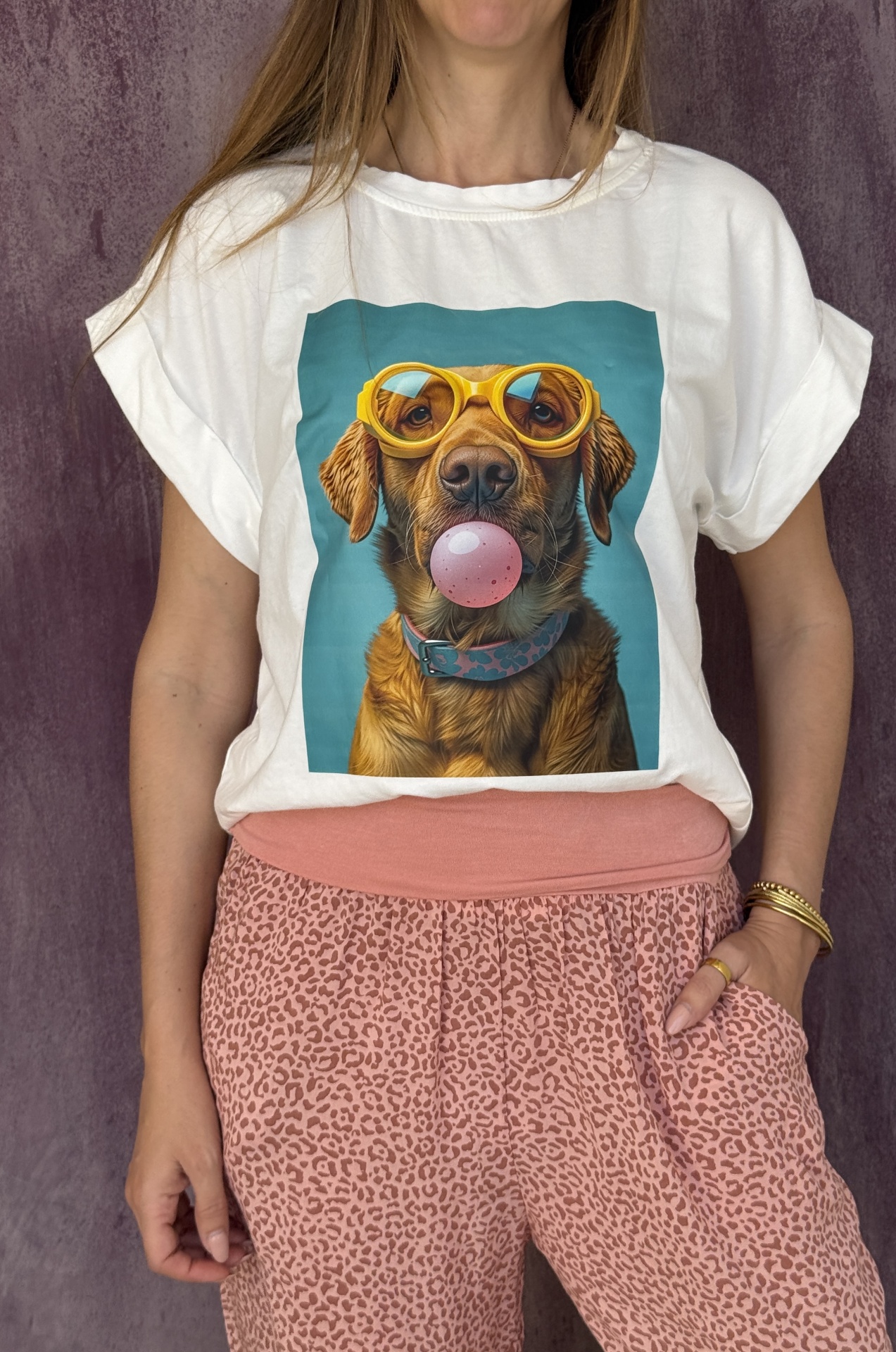 Pessoa com t-shirt branca com estampa de cão com óculos amarelos e chiclete cor-de-rosa, e calças rosa com padrão animal print