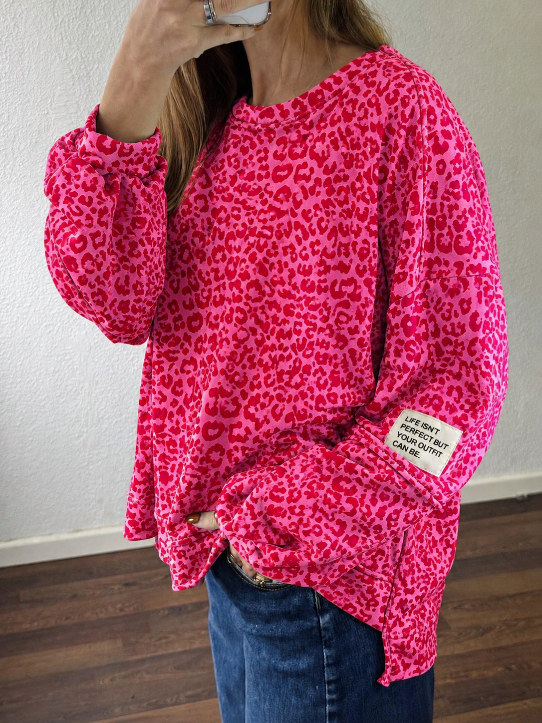 Camisola rosa com padrão animal print e etiqueta na manga, usada com calças de ganga.