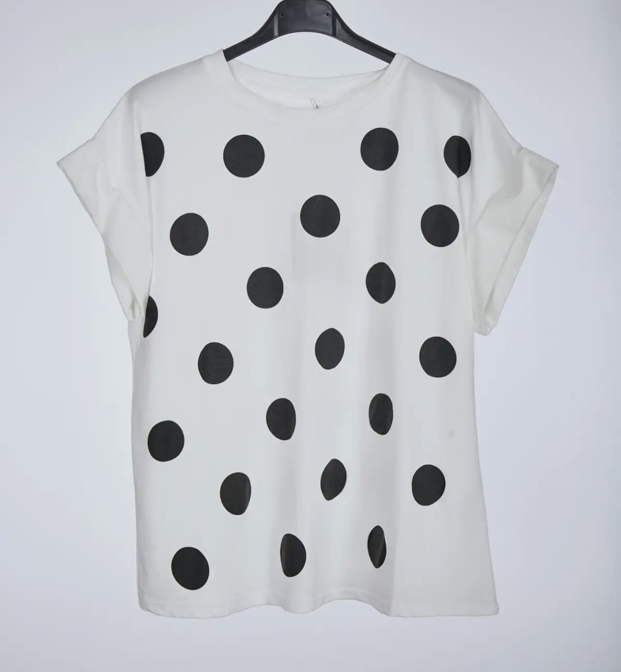 T-shirt branca com bolinhas pretas e mangas curtas num cabide
