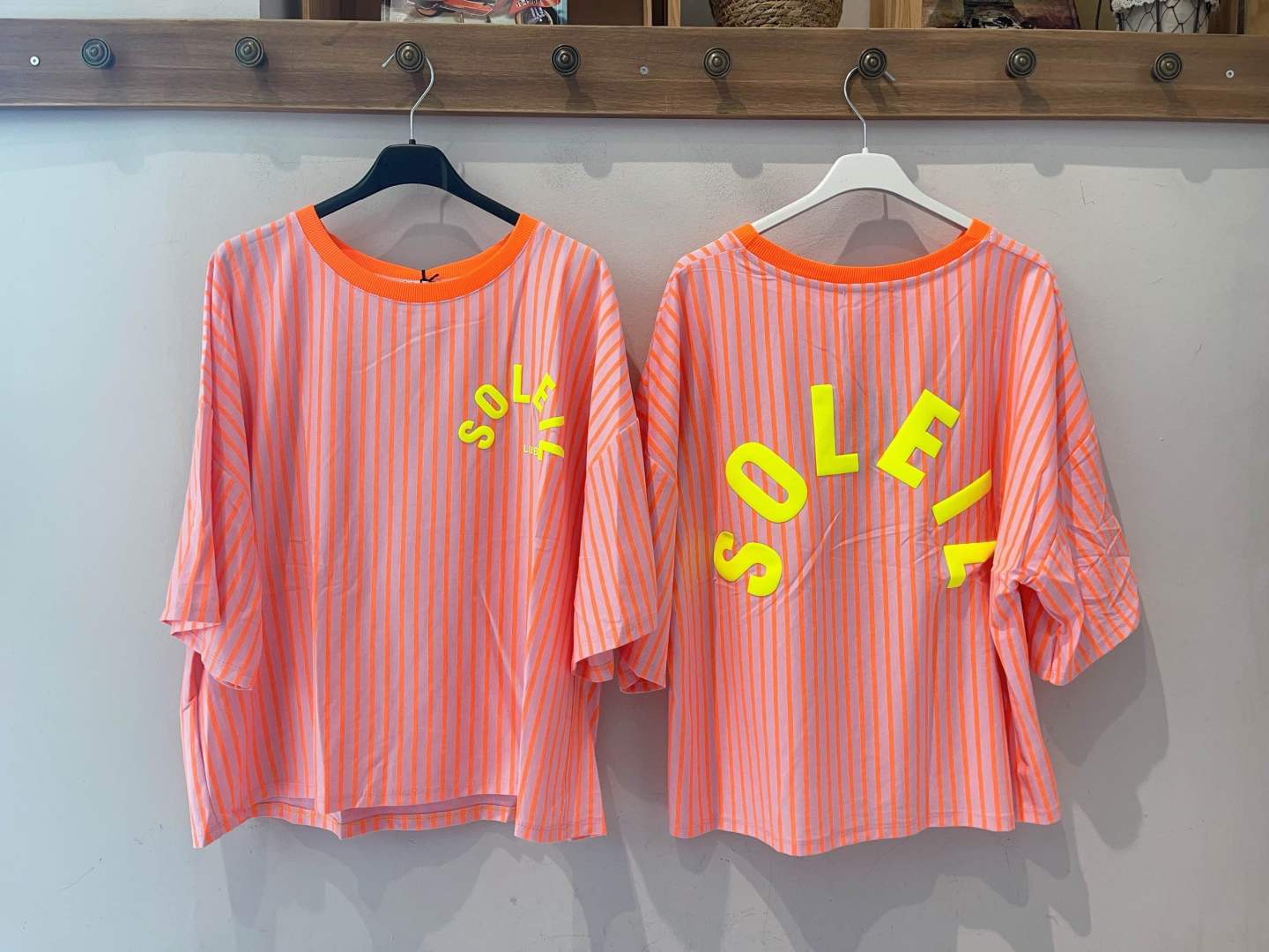 Duas t-shirts às riscas rosa e laranja com palavra amarela fluorescente SOLFIL penduradas num cabideiro