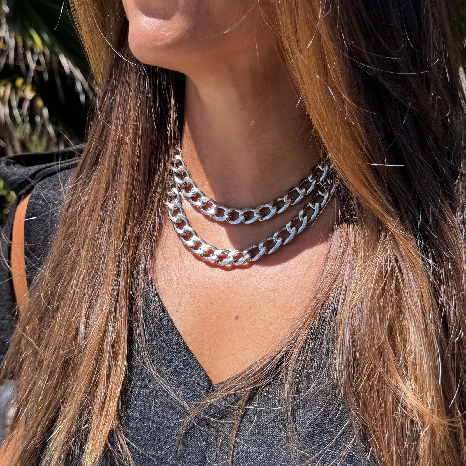 Colar duplo tipo corrente grossa em metal prateado no pescoço de mulher.