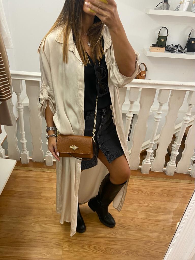 Mulher com casaco longo bege claro, vestido preto, botas pretas e mala castanha numa loja