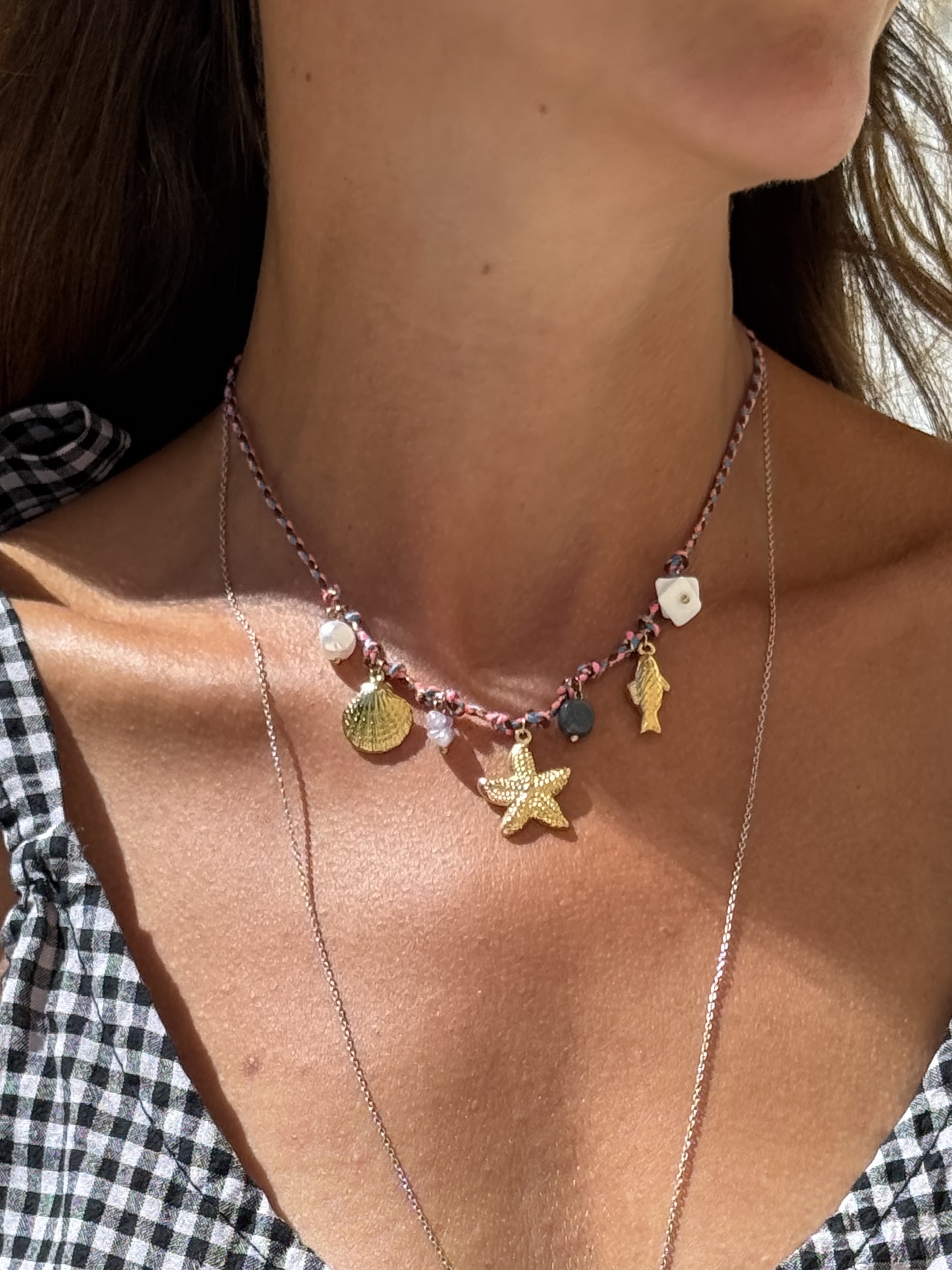 Colar trançado com pendentes dourados e contas em pescoço de mulher com vestido xadrez