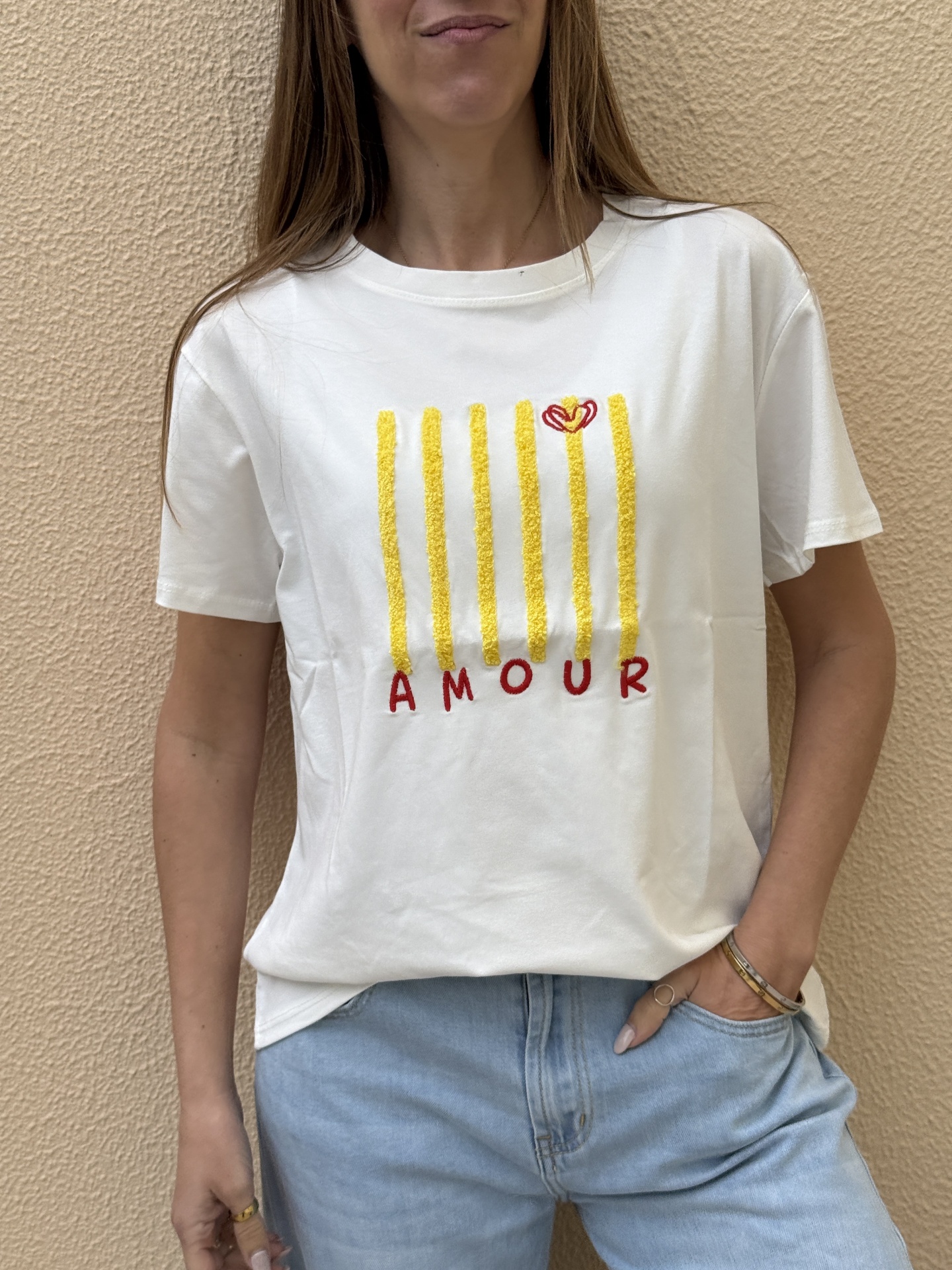 T-shirt branca com riscas amarelas e texto AMOUR vermelho