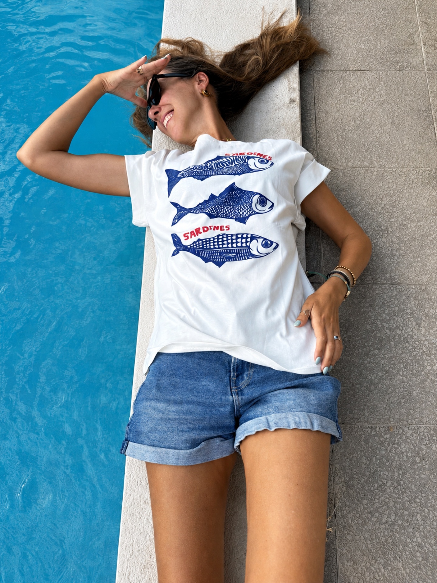 Pessoa deitada junto à piscina com t-shirt branca e calções de ganga azuis