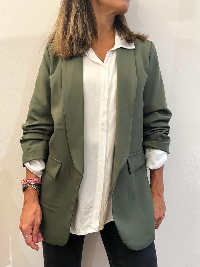 Mulher a usar blazer verde musgo, camisa branca e calças pretas em fundo branco