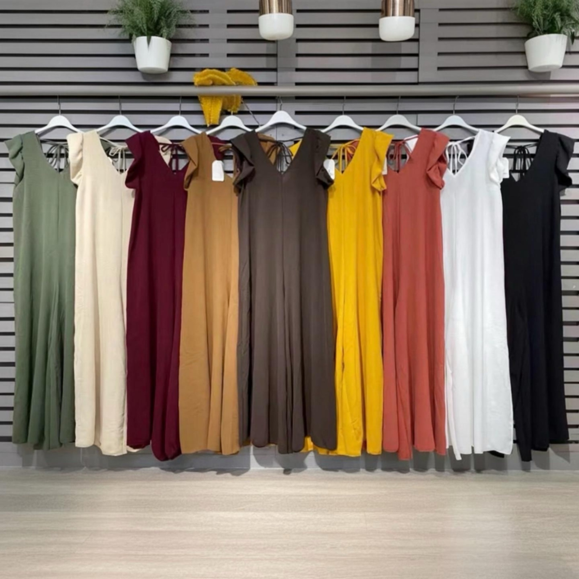 Vestidos coloridos pendurados em cabides brancos em frente a painéis cinzentos horizontais