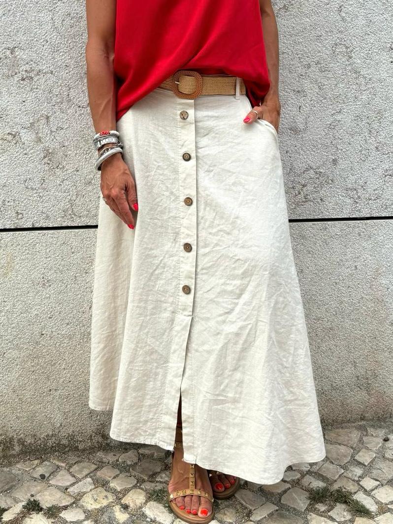 Saia comprida bege com botões à frente e cinto bege, blusa vermelha, sandálias castanhas, pavimento de pedra e parede cinza clara