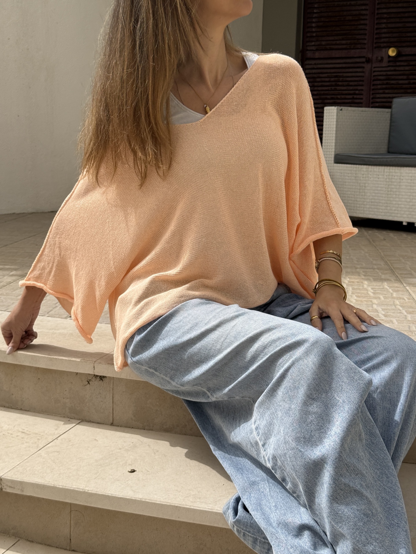 Pessoa sentada em escadas vestindo camisola pêssego de malha e calças largas de ganga azul clara