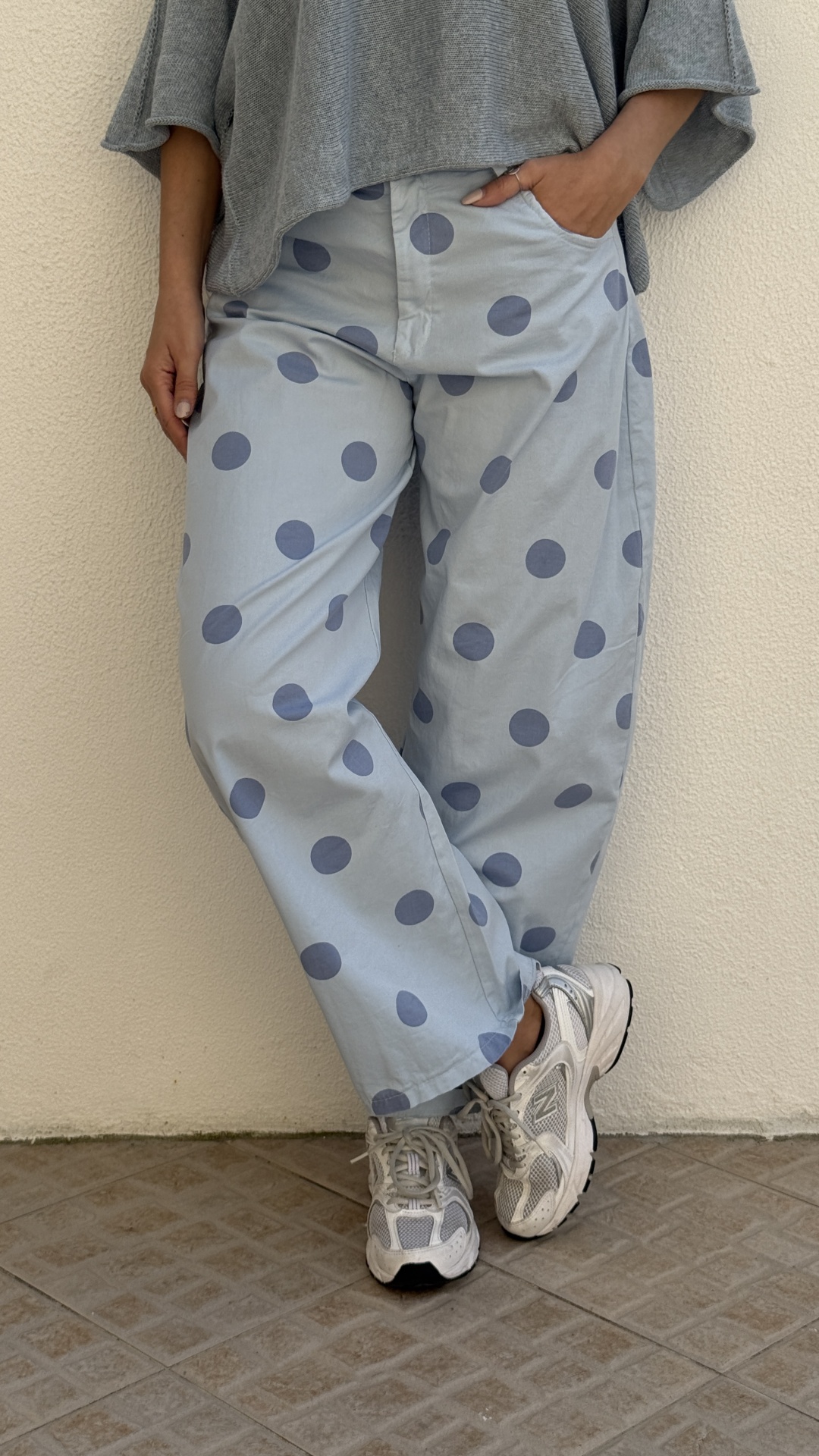 Calças compridas azul claro com bolinhas azuis, ténis brancos e camisola cinzenta