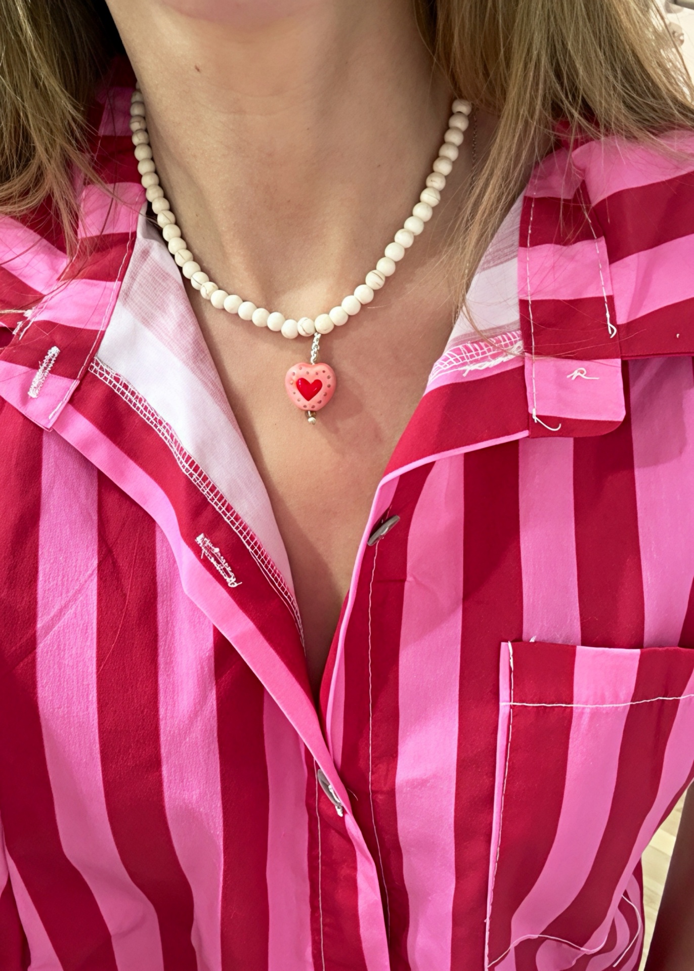 Colar com conta em forma de coração rosa e camisa às riscas rosa e vermelha