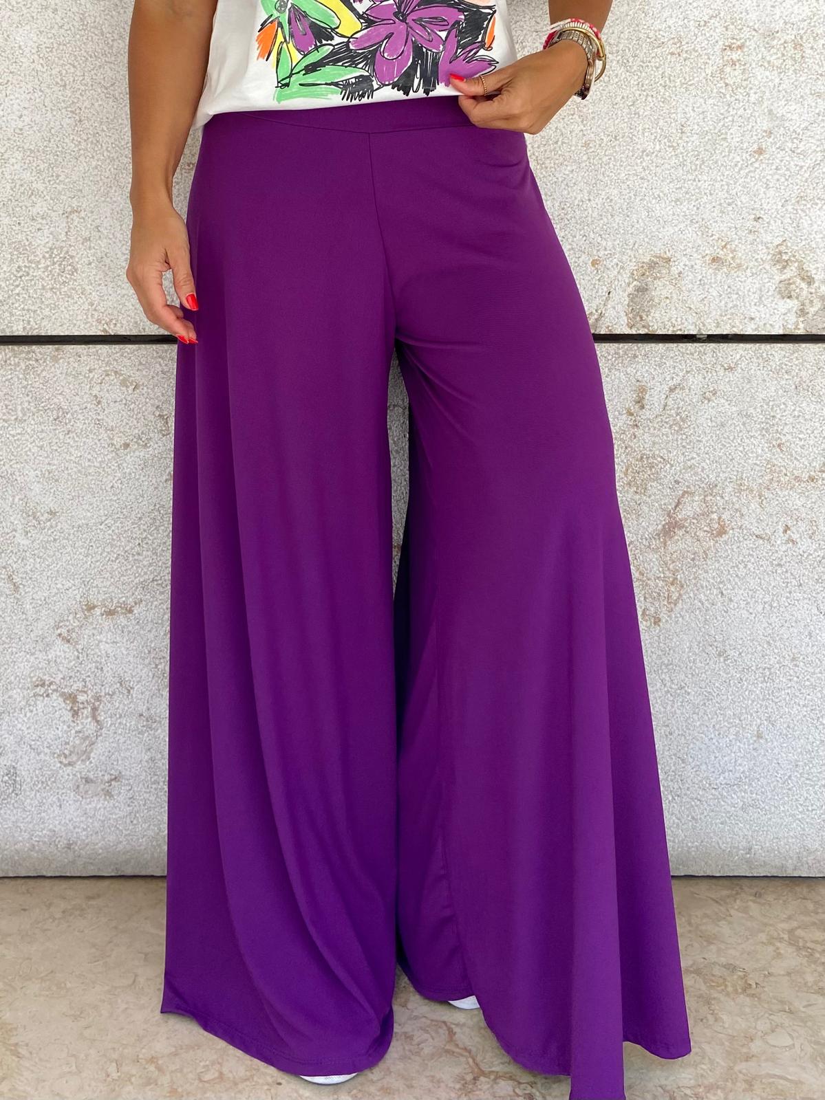Calças largas roxas em tecido fluido junto a parede clara
