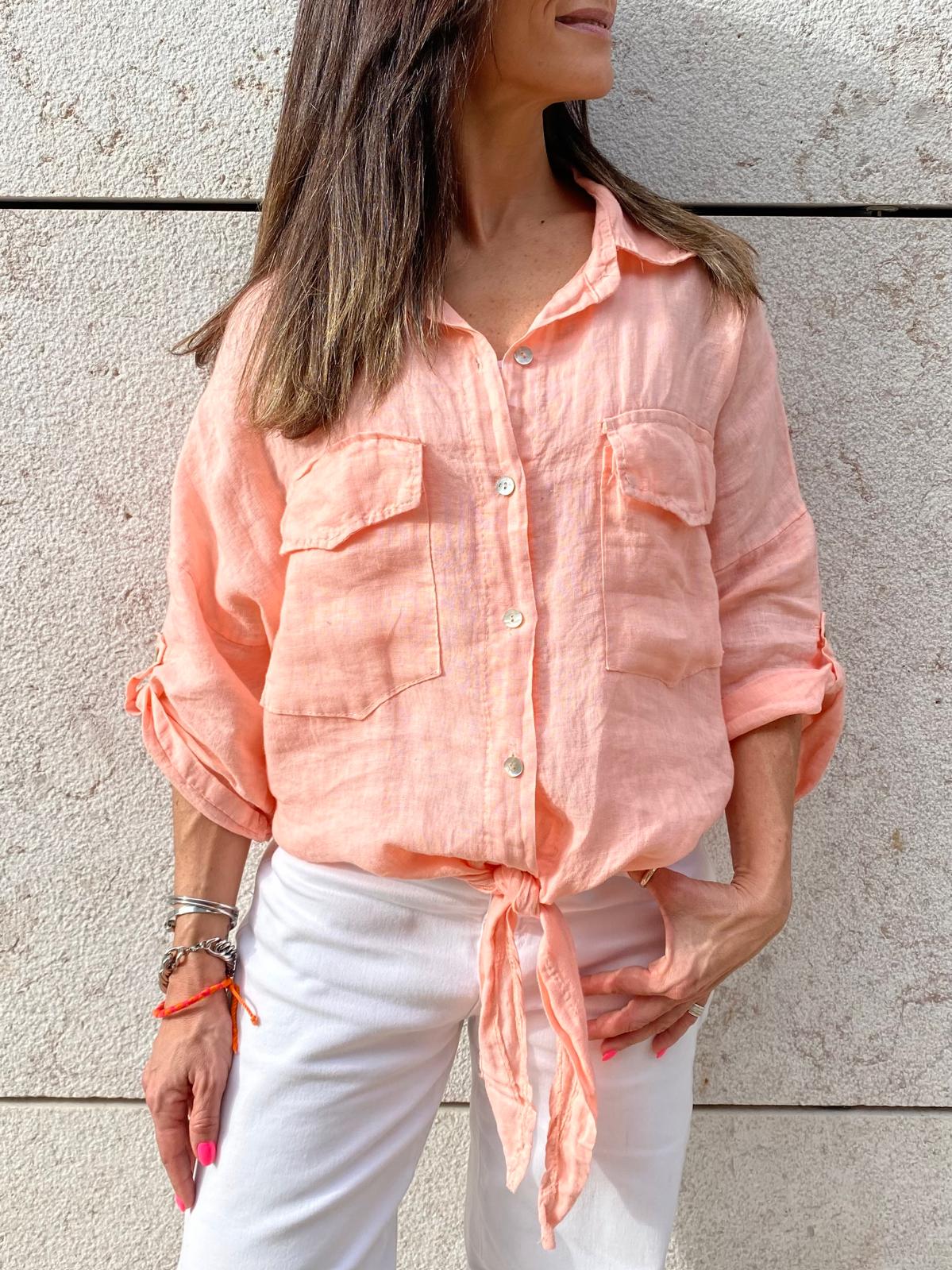 Camisa feminina salmão com botões e bolsos, usada com calças brancas, parede clara ao fundo