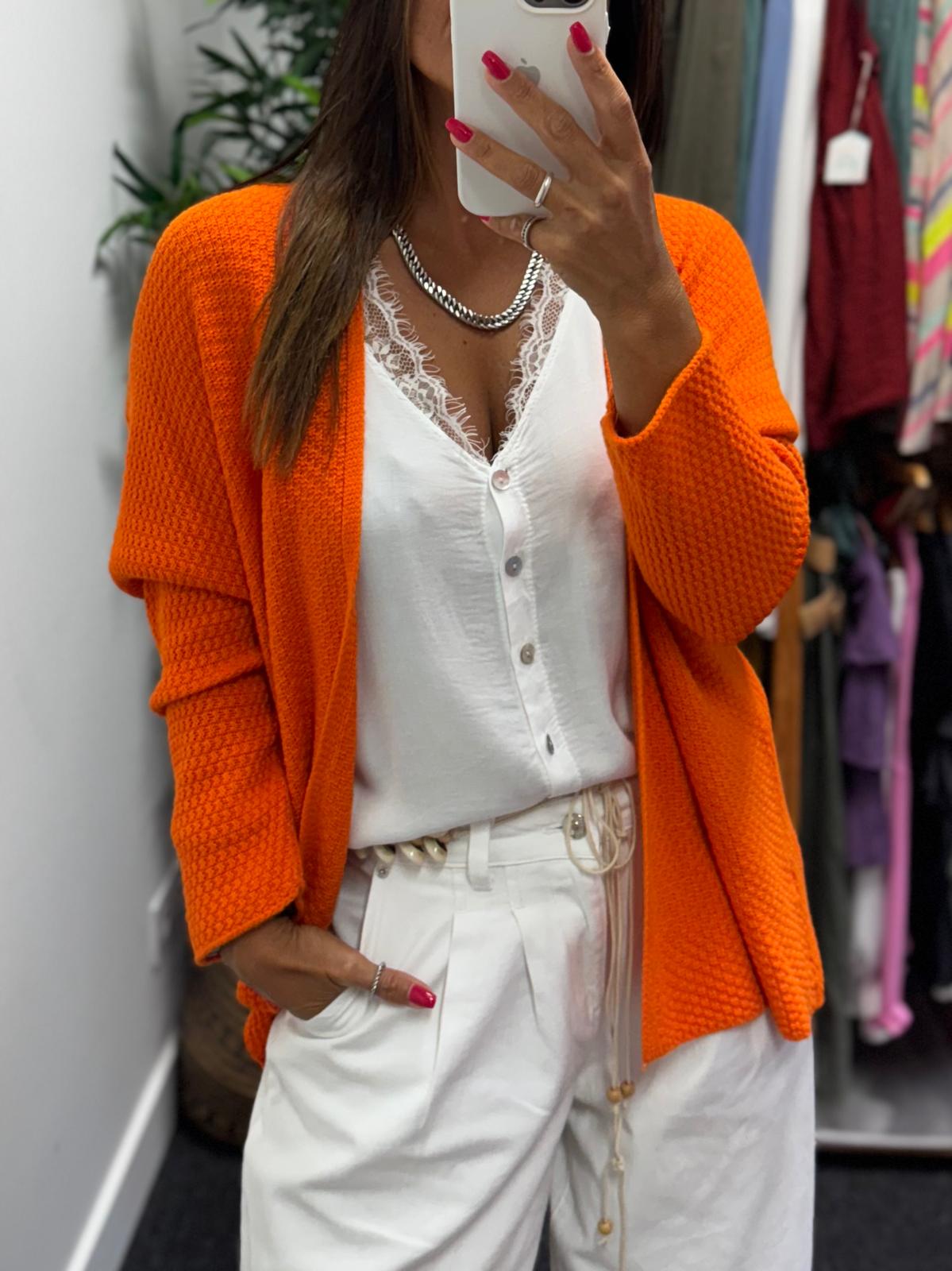 Cardigã laranja de malha com blusa branca e calças brancas em ambiente interior