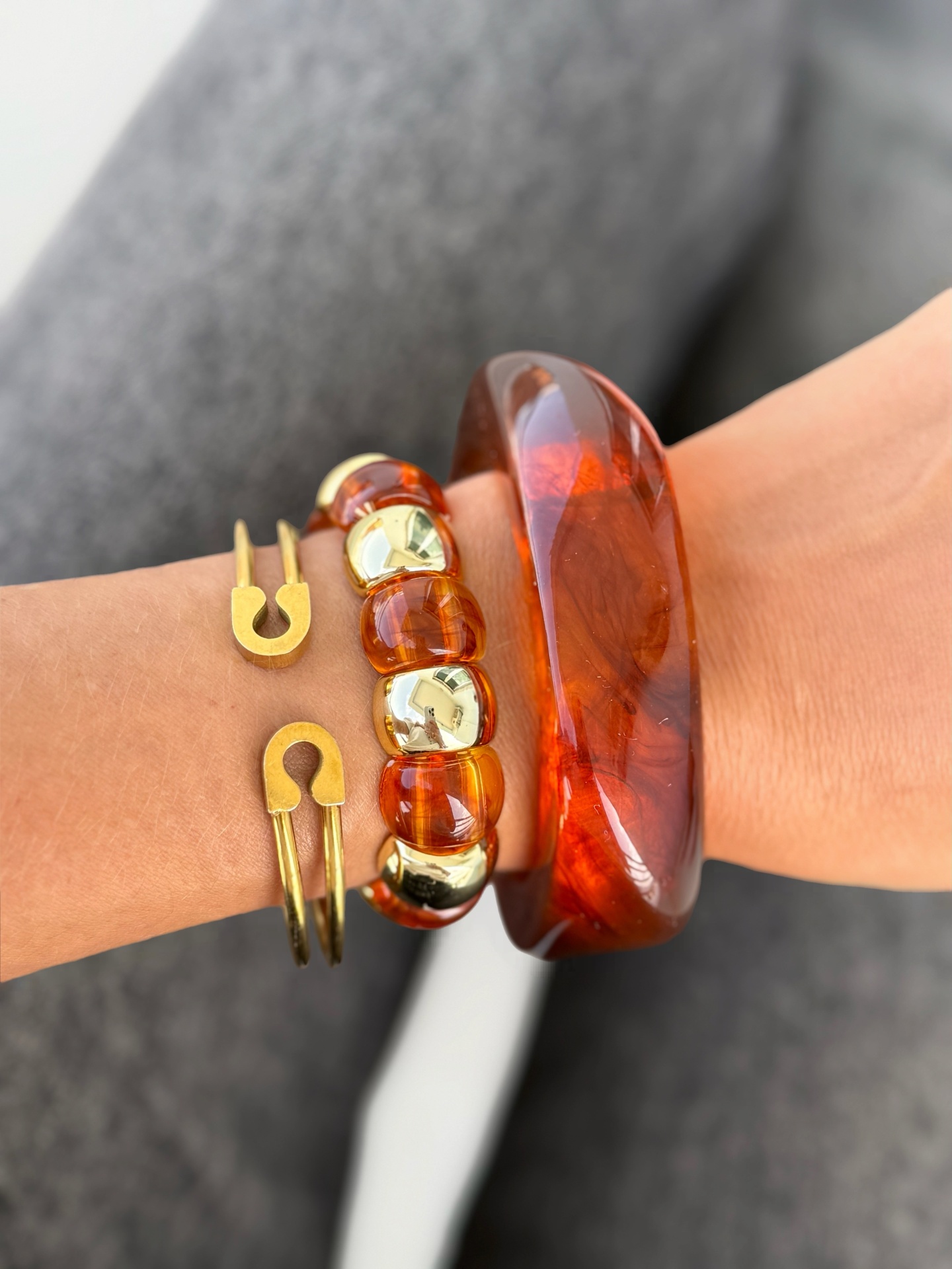 Três pulseiras, castanha translúcida, castanha com dourado e dourada minimalista, num pulso com fundo cinzento desfocado