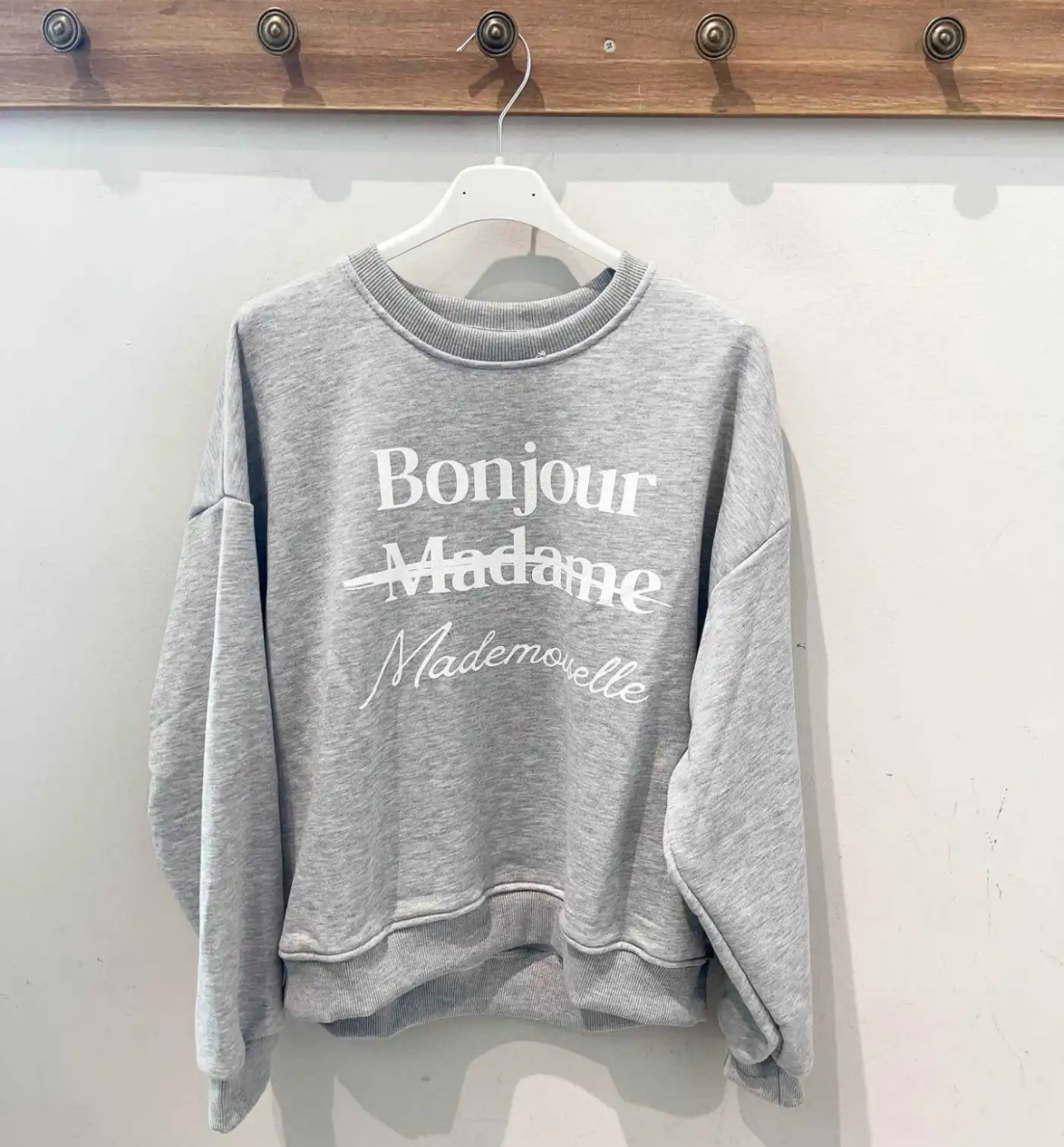 Sweatshirt cinza claro com texto branco pendurada num cabide branco.