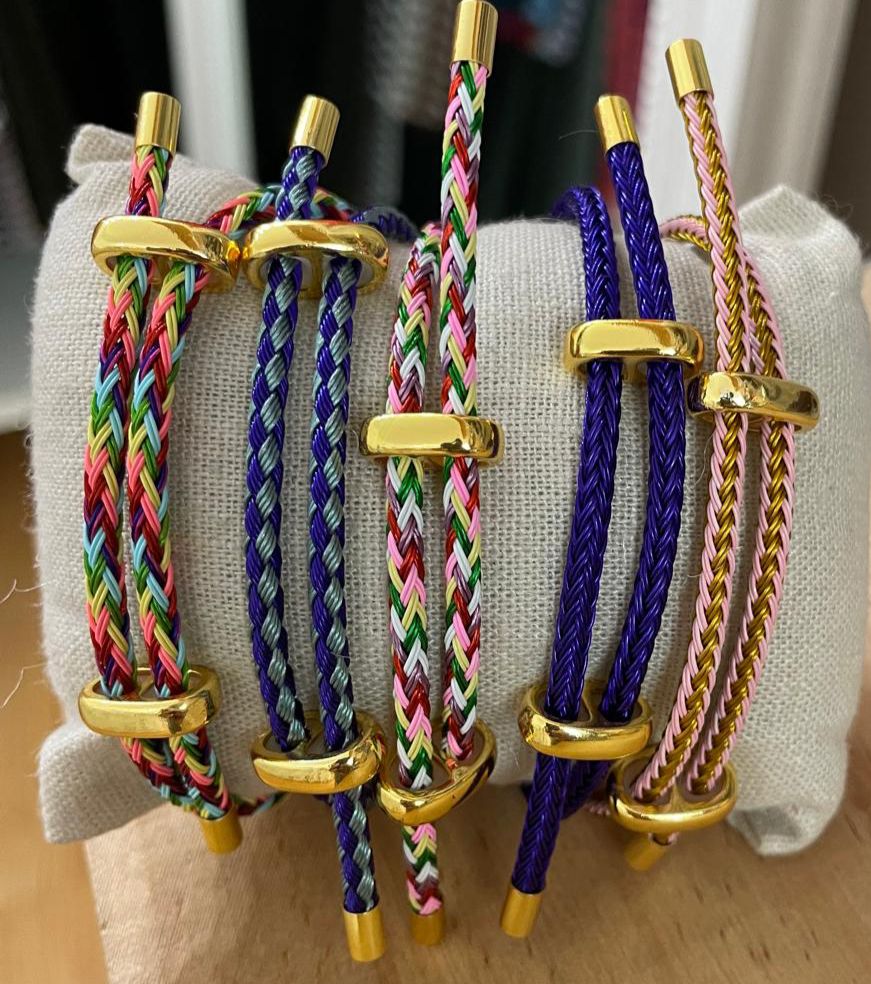 Pulseiras trançadas coloridas com detalhes dourados em suporte de tecido