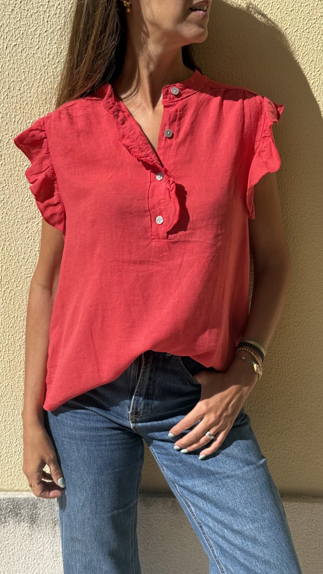 Blusa vermelha de folhos com botões e calças de ganga azuis em fundo de parede amarela