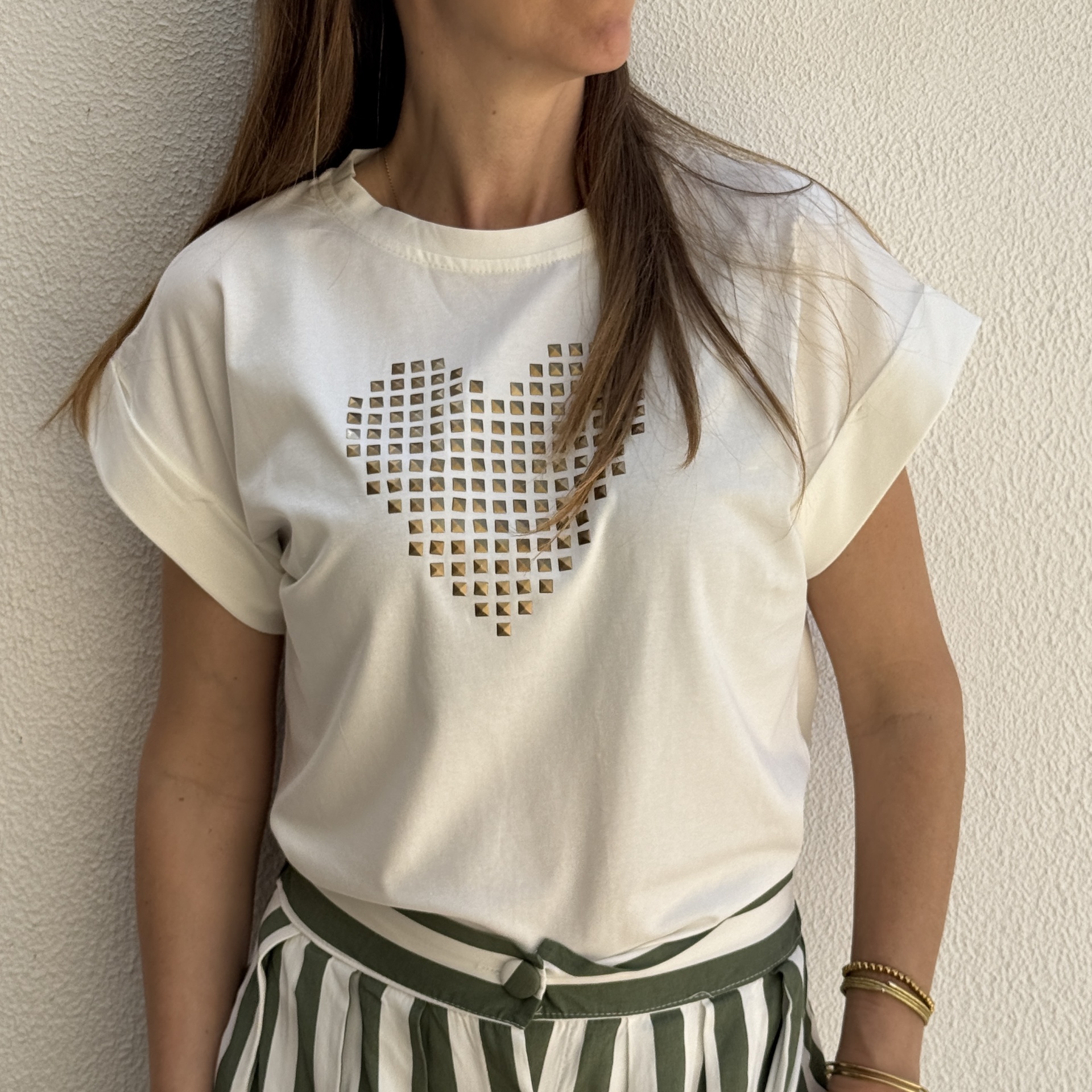 T-shirt branca com coração dourado e saia/calças listradas verdes e brancas.