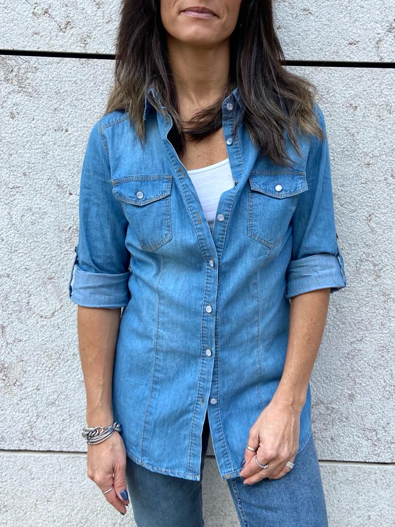 Camisa de ganga azul clara com botões e bolsos no peito, usada por mulher contra parede clara