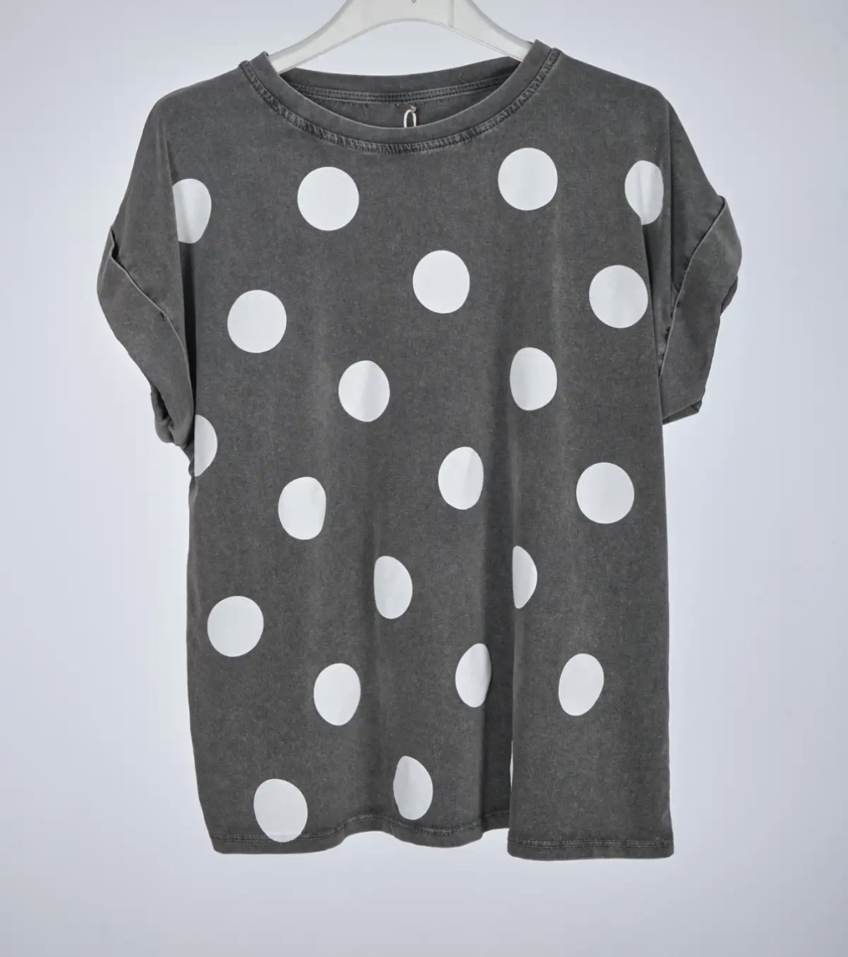 T-shirt cinzenta com bolas brancas grandes e mangas curtas enroladas pendurada num cabide branco