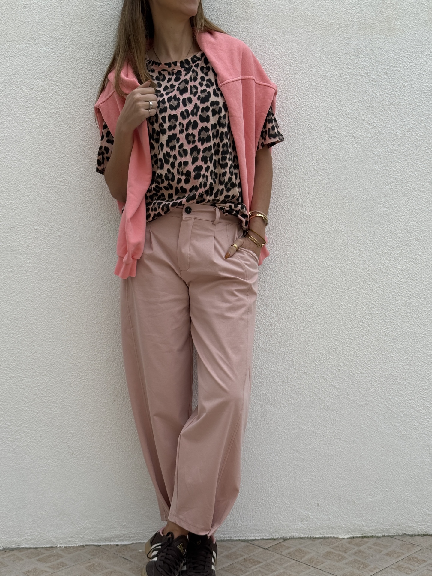 Modelo vestindo t-shirt animal print, camisa rosa, calças rosa claras e ténis pretos com riscas brancas em fundo branco.