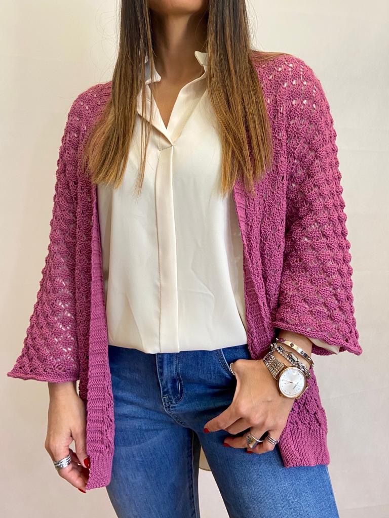 Pessoa com camisola rosa de malha aberta, camisa branca e calças de ganga azuis.