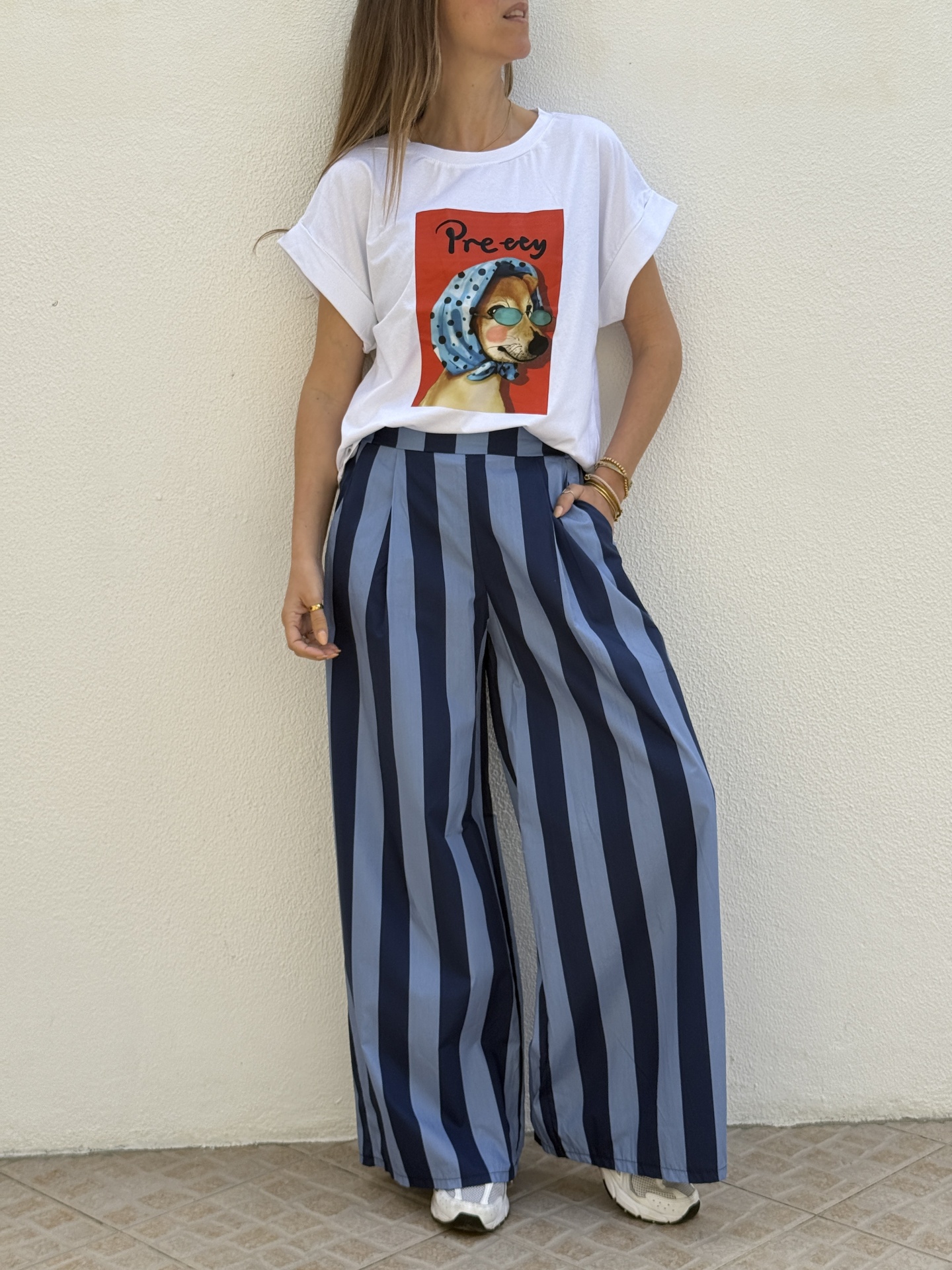 Mulher veste t-shirt branca com estampa de cão e calças largas às riscas azuis