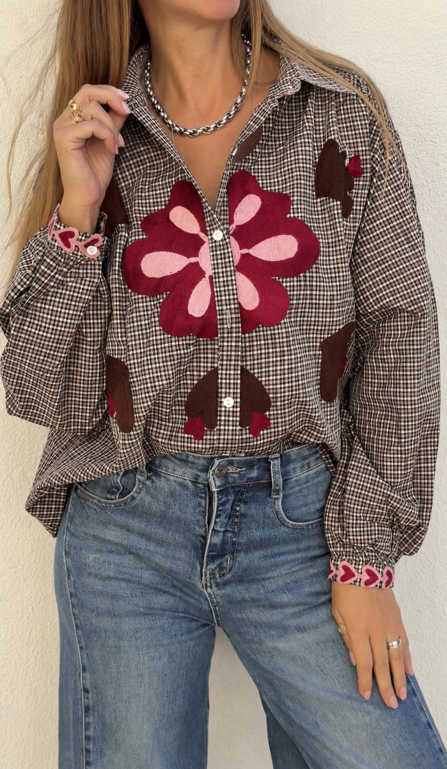 Blusa xadrez castanha com bordados florais cor-de-rosa e vermelhos, usada com calça de ganga azul claro.