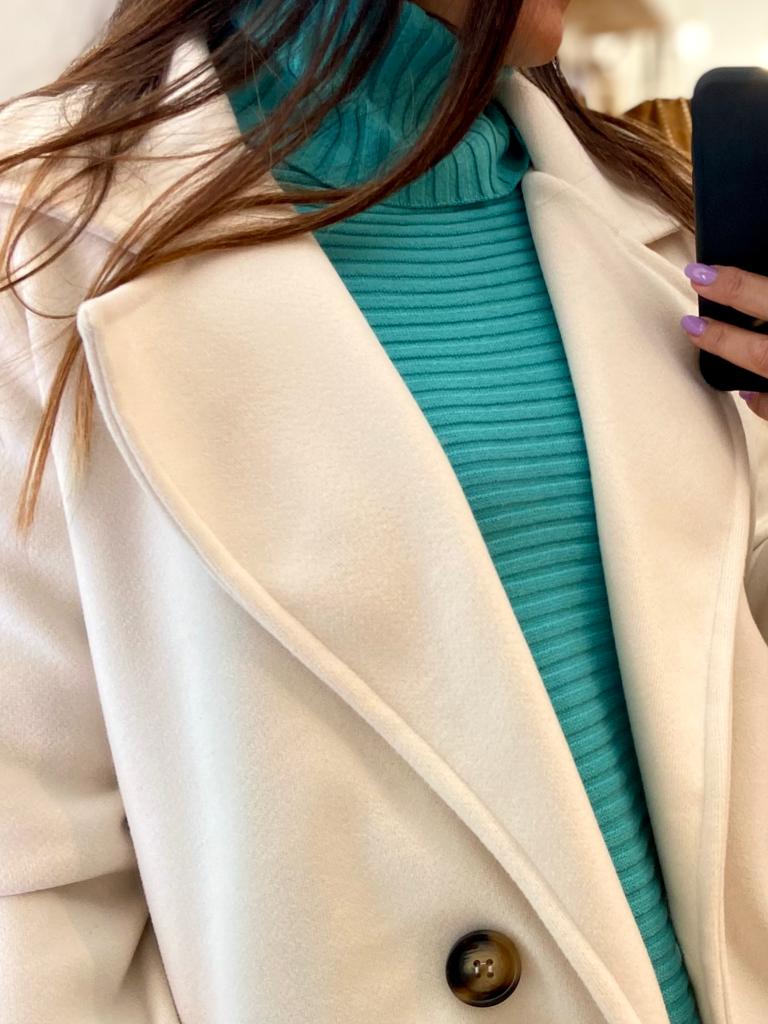 Casaco bege com gola larga sobre camisola azul turquesa de gola alta