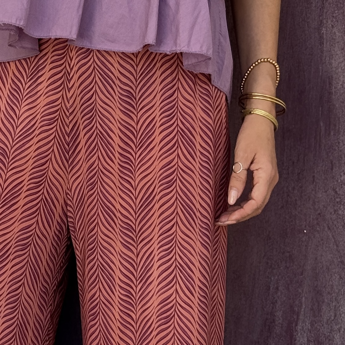 Calças com padrão laranja e púrpura e blusa lilás com pulseiras douradas
