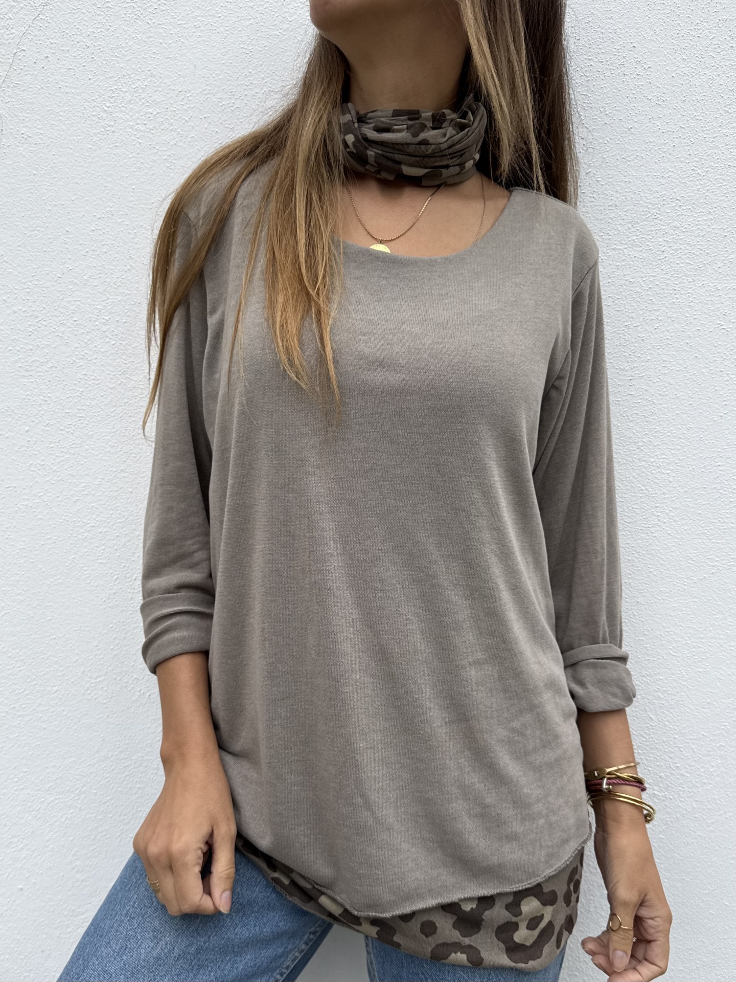 Pessoa com camisola castanha, lenço camuflado e calças de ganga