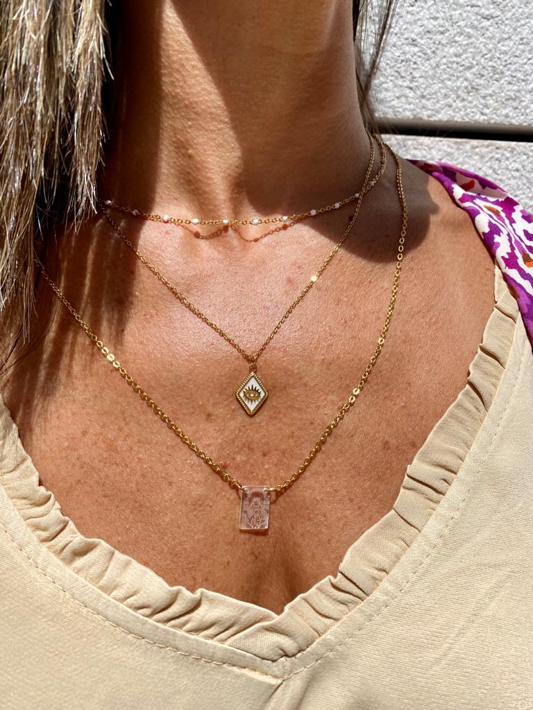 Colares dourados em pescoço de mulher com vestido bege e detalhe de tecido roxo estampado no ombro