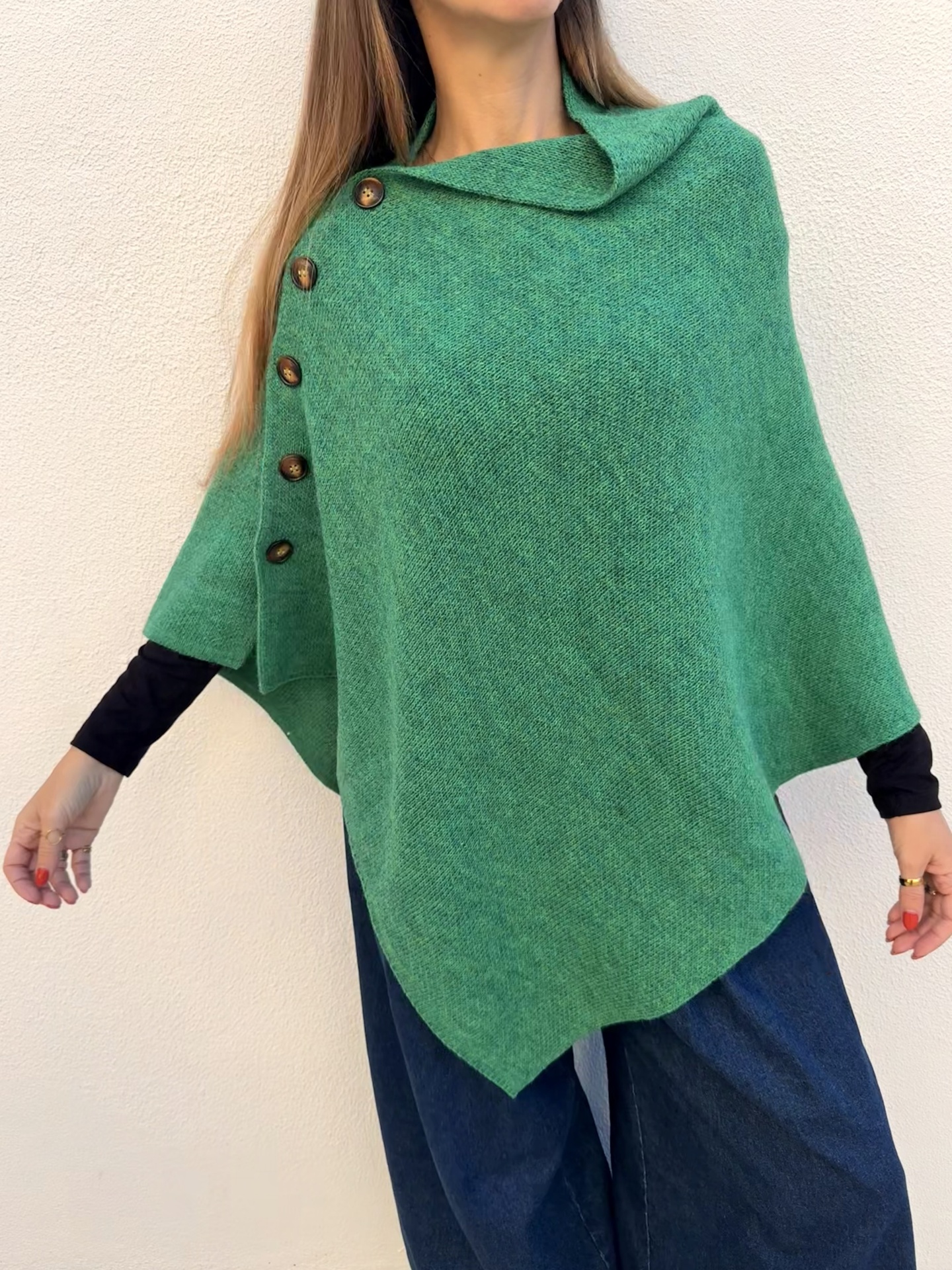 Poncho verde com botões castanhos usado sobre camisa preta e jeans