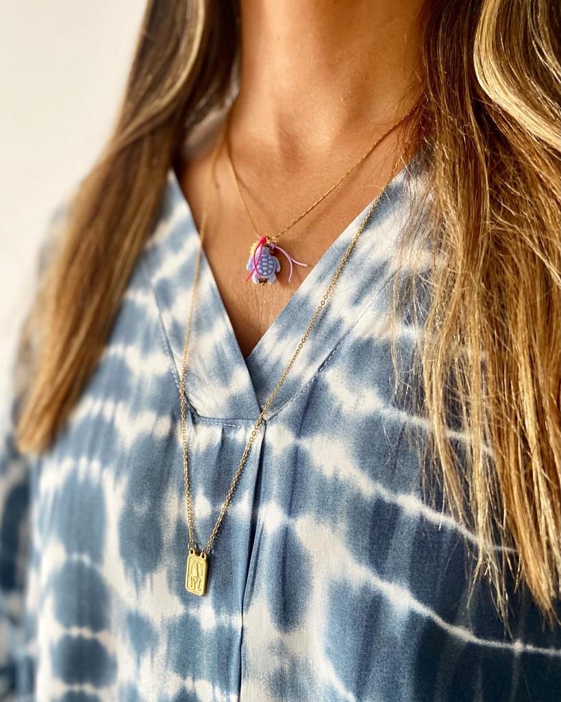 Colar duplo dourado com pedras e placa retangular em pessoa com blusa azul tie-dye