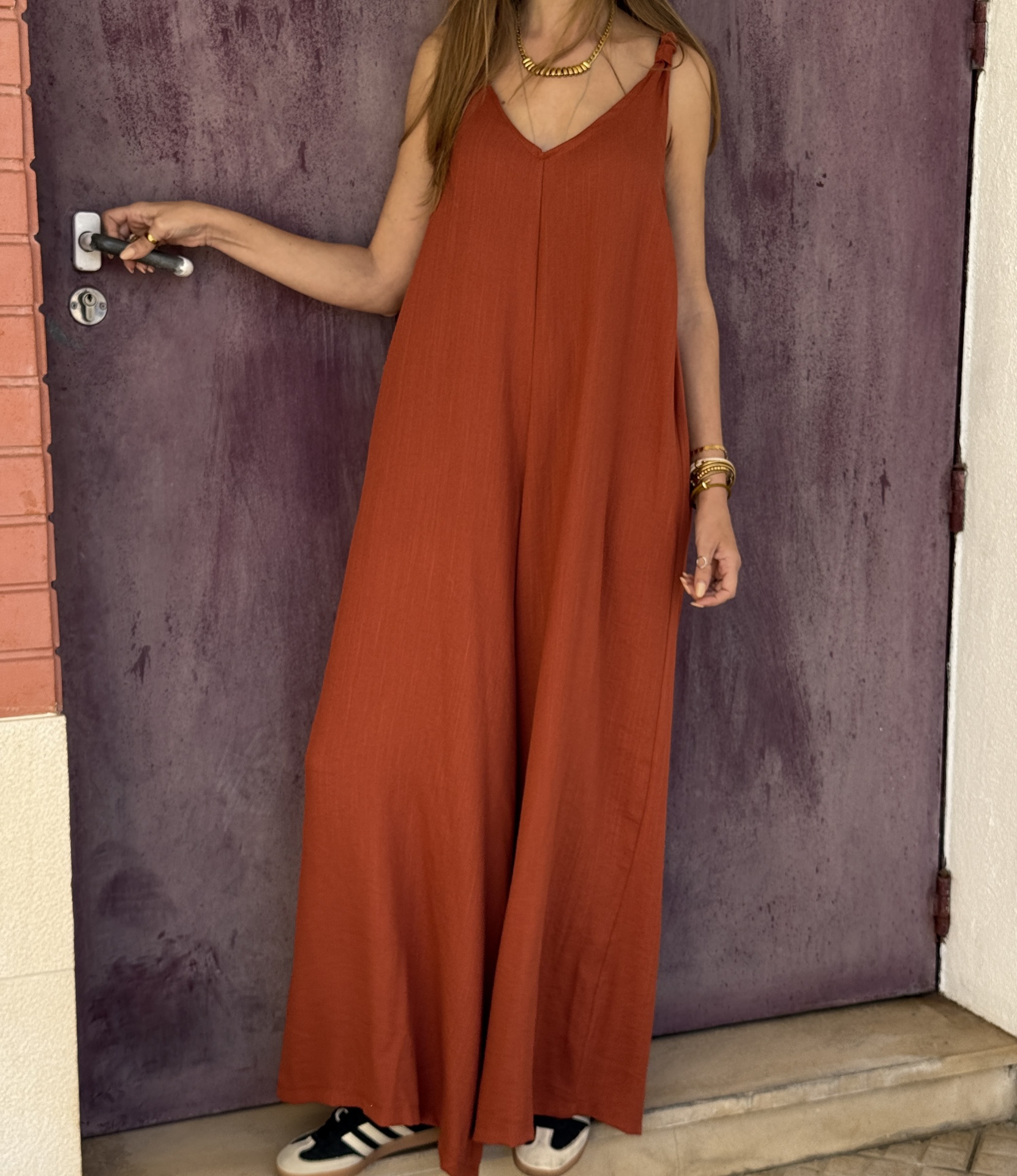 Macacão largo laranja em mulher junto a porta roxa com maçaneta metálica