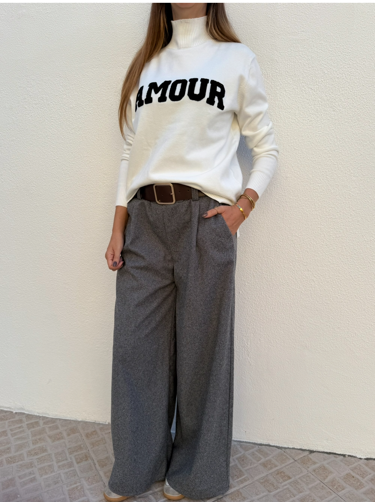 Pessoa a usar sweat branca com texto AMOUR preto e calças largas cinza com padrão espinha de peixe