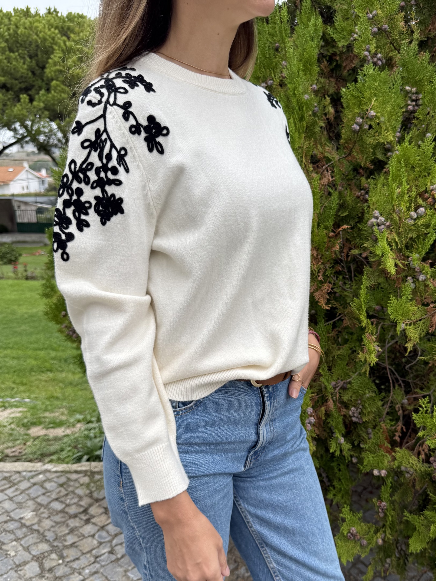 Camisola branca com padrão floral preto nos ombros e jeans azuis exterior