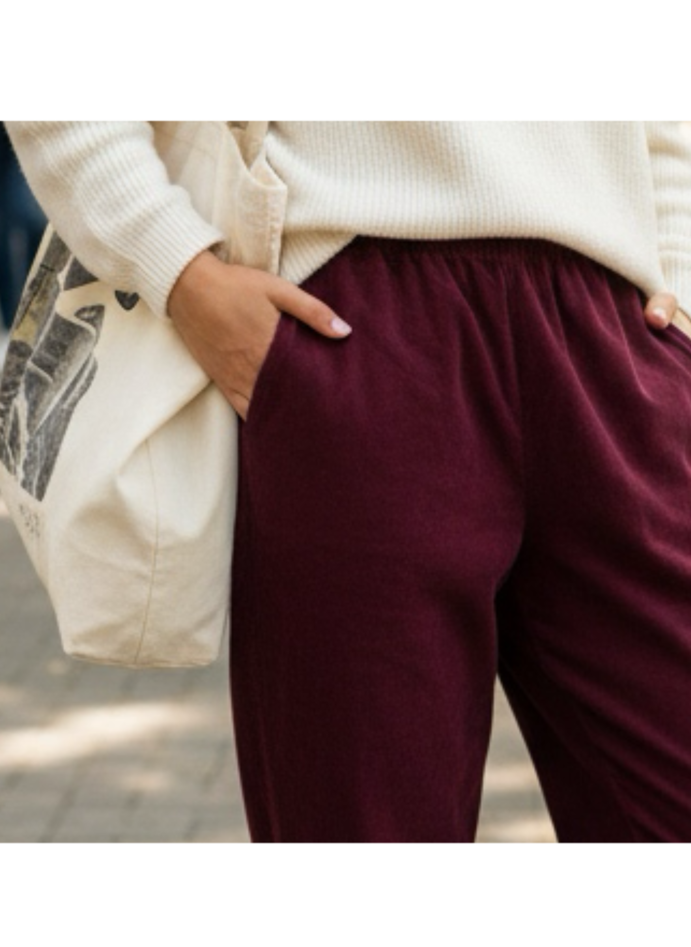 Calças bordeaux com cós elástico, casaco branco de malha e mala de tecido com estampa preta