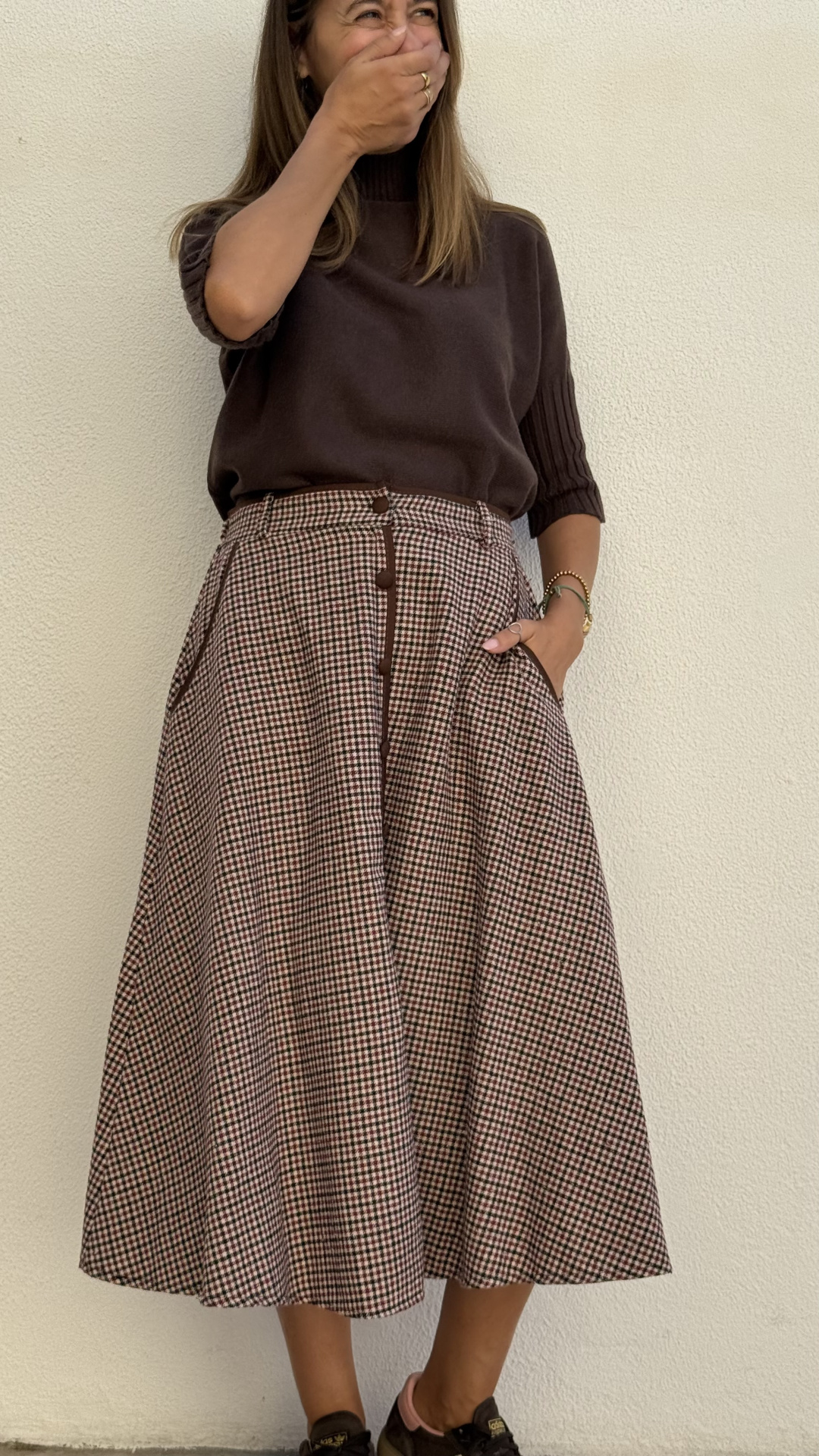 Mulher com camisola castanha e saia xadrez rodada