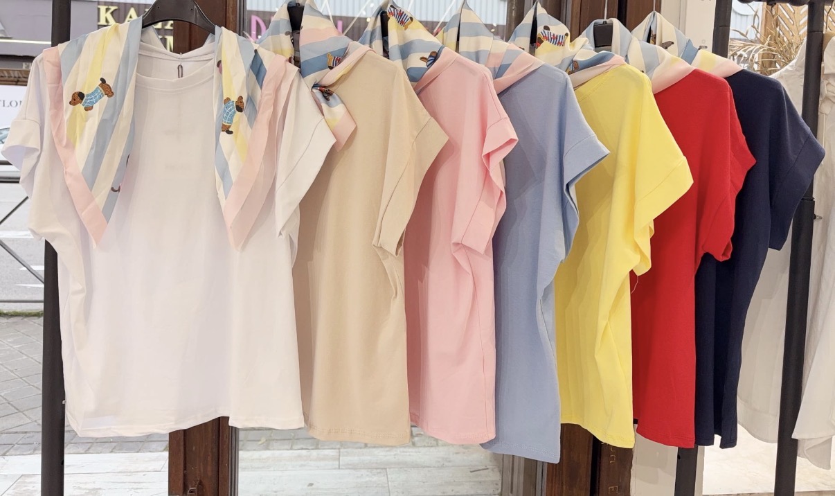 Sete t-shirts de várias cores com lenços coloridos penduradas em cabides