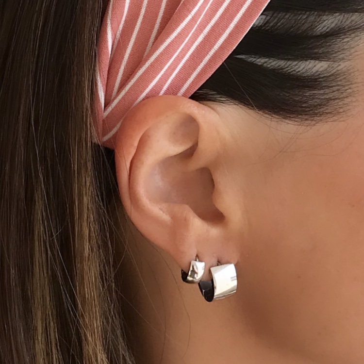 Brinco de argola dupla prateada usado na orelha de mulher com faixa rosa de riscas brancas