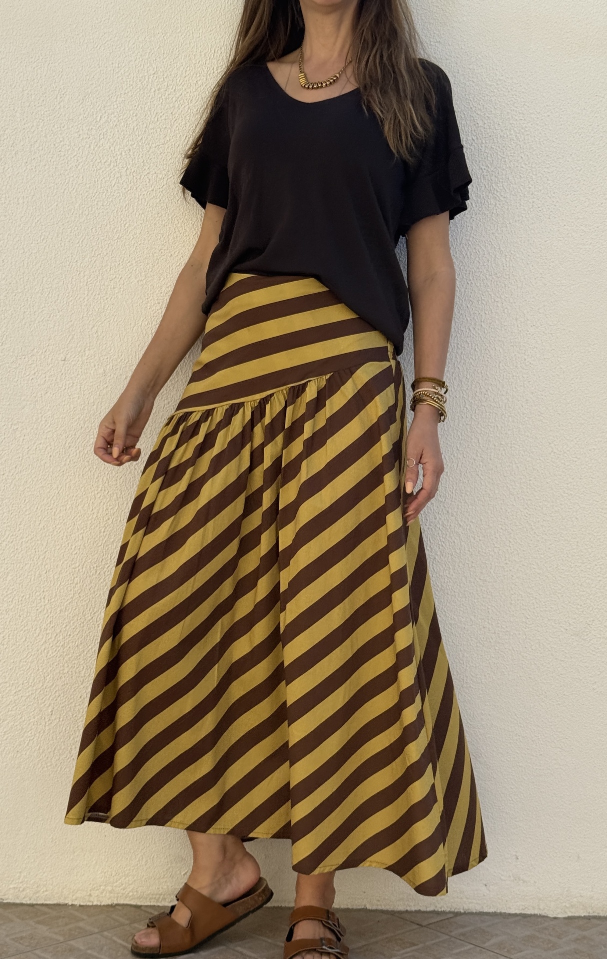 Saia longa às riscas amarelas e castanhas e blusa preta com folhos