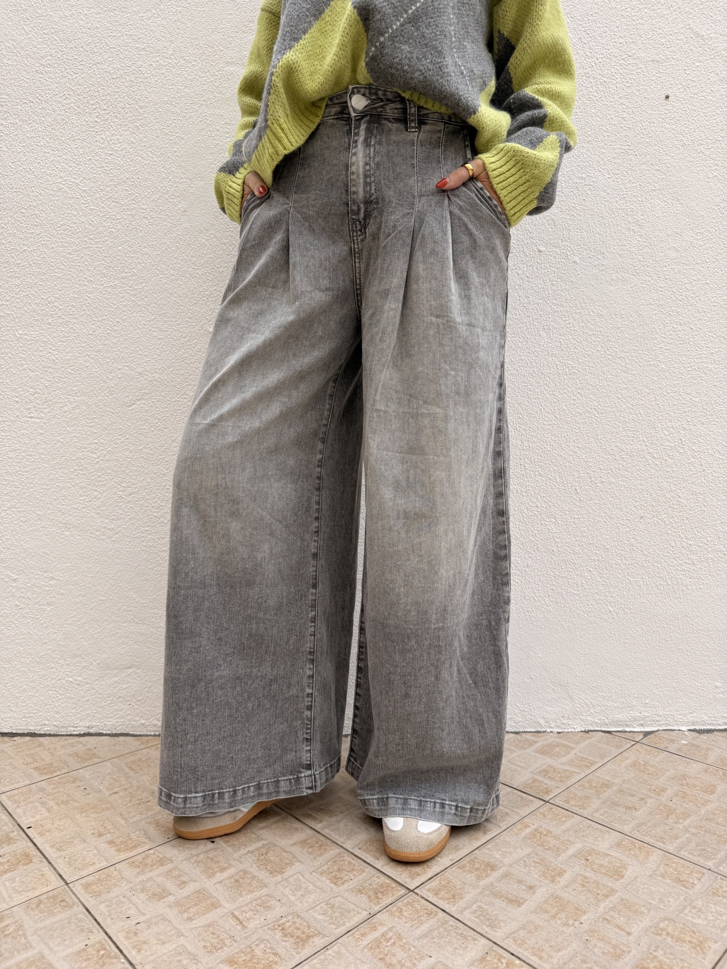 Calças largas de ganga cinza lavado com camisola amarela e cinza, sapatilhas claras, parede branca