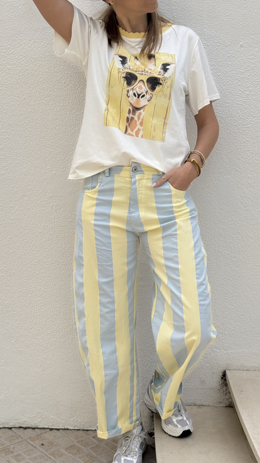 Calças às riscas azul claro e amarelo com t-shirt branca estampada com girafa de óculos.