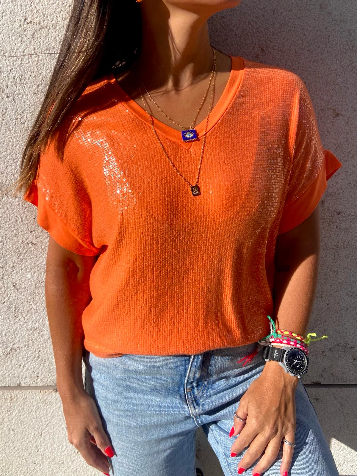 Pessoa a usar camisola de malha laranja com jeans claros e acessórios coloridos