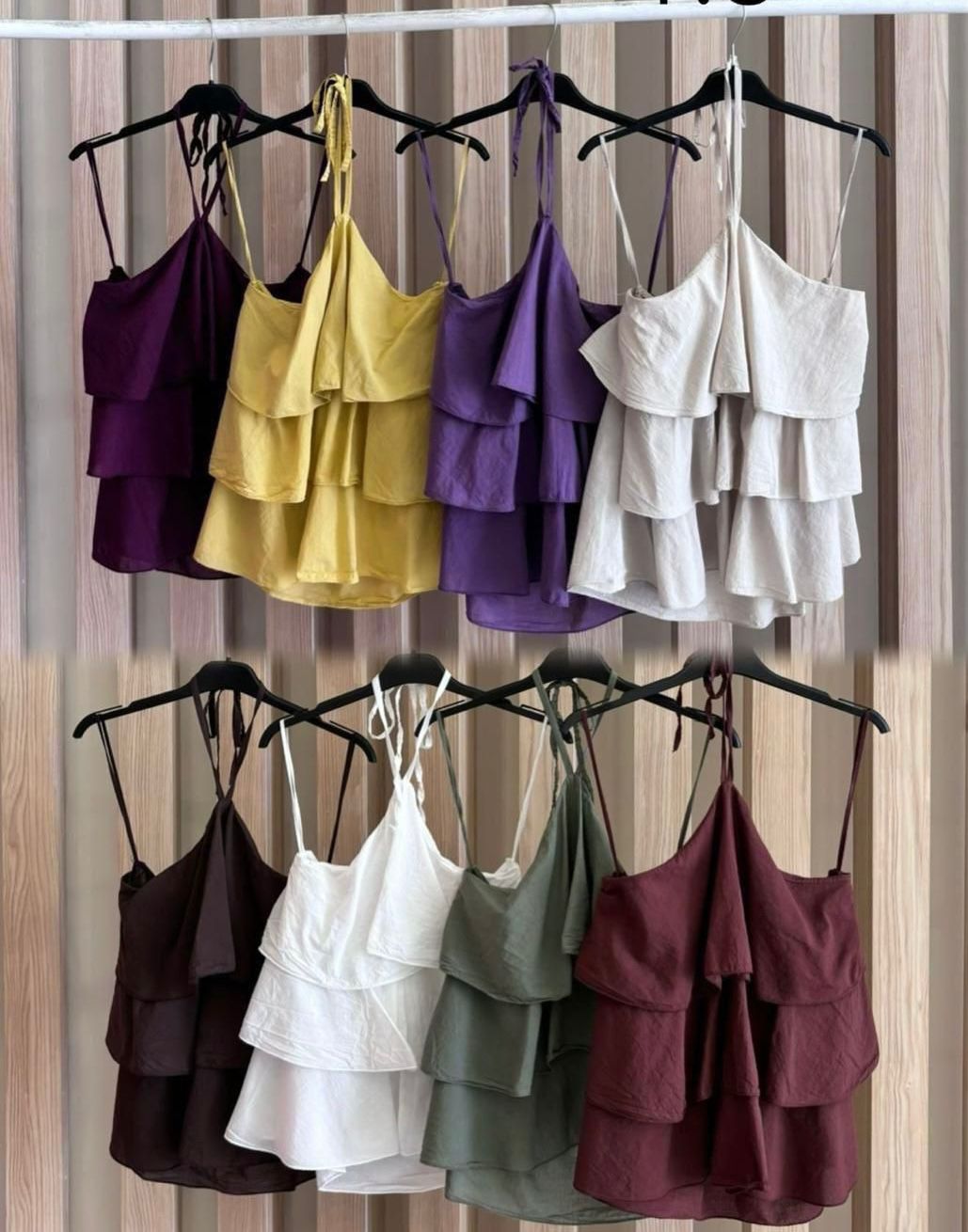 Oito blusas de alças finas colores variadas com padrão de camadas penduradas em cabides pretos